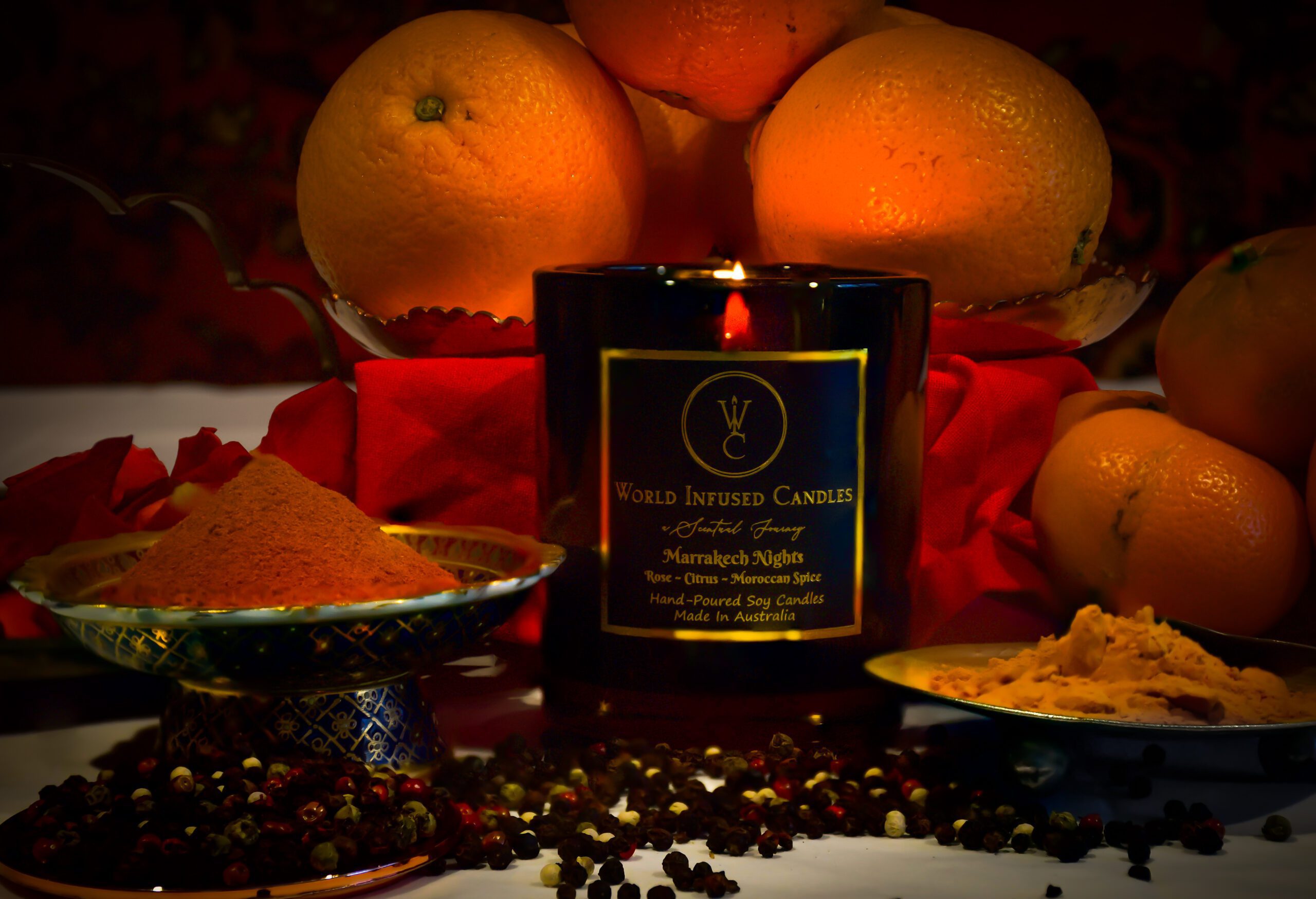 Marrakech Nights Soy Candle lit with spices in the foreground. the background is filed with citrus fruits and rose petals